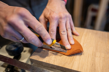 Man hands cutting leather skin. Master shoemaker pro cobbler guy palms measures right amount, uses ruler tool retractable construction knife. Process of working with natural leather in workshop