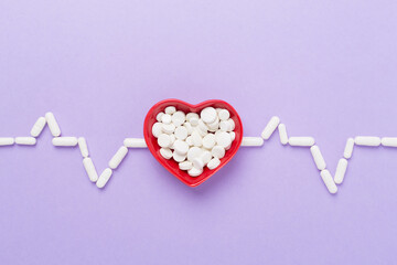 Cardiogram made with medicines and heart-shaped bowl on color background, top view