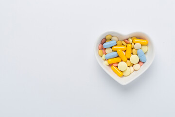 Fototapeta na wymiar Medicines in heart-shaped bowl on color background, top view