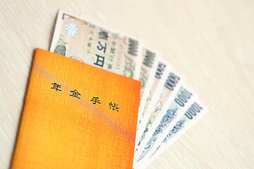 Japanese pension insurance book on table with yen money bills. Orange book for japan pensioners close up