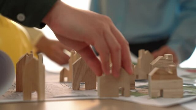 Architect and engineer discuss about building blueprint on table with architectural document, measurement tools scatter around at office, use wooden block for house positioning. Closeup. Delineation.