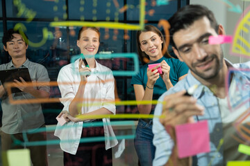 Professional businessman writing on glass wall at night office while coworker listening carefully. Group of business team working together,brainstorming, sharing marketing idea. Business plan.Tracery.