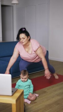 Overweighted woman performing yoga asana warrior at home with her baby on the floor