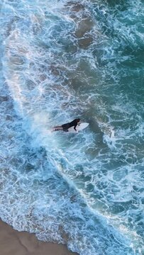 Aerial vertical slow-motion of surfer running into the sea at Tamarama beach Sydney in Australia