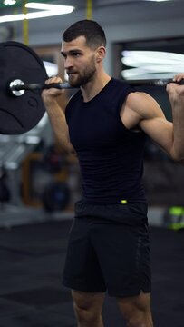 Muscular man training with barbell, doing squats in gym