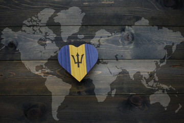 wooden heart with national flag of barbados near world map on the wooden background.