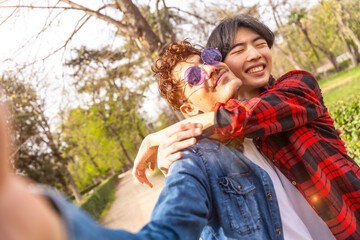 Gay couple taking selfie embracing in a park - obrazy, fototapety, plakaty