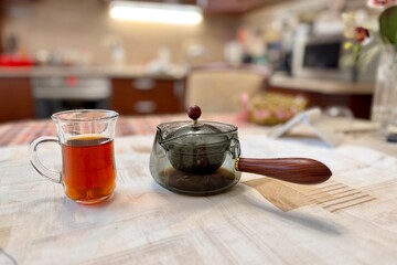 A glass vessel in the form of a mug with delicious dark tea standing on the table with a glass...