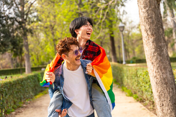 Fototapeta premium Happy gay couple piggybacking and laughing in a park