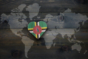wooden heart with national flag of dominica near world map on the wooden background.