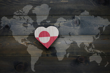 wooden heart with national flag of greenland near world map on the wooden background.