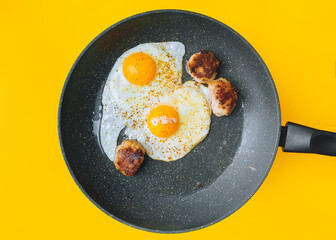 Scrambled eggs in a frying pan next to three cutlets on a yellow background. Breakfast, lunch and dinner concept for student or bachelor.