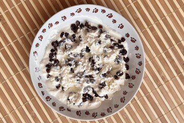 Cottage cheese with black raisins on a white breakfast plate for a healthy diet in background light...
