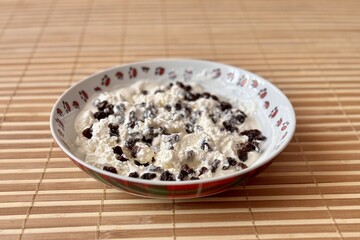 Cottage cheese with black raisins on a white breakfast plate for a healthy diet in background light bamboo. Close-up