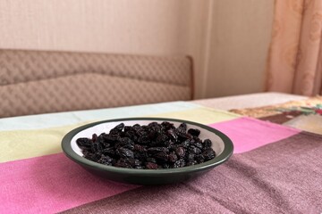A lot of black raisin in the white green plate is located on the table at home. Close-up