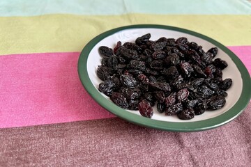 A lot of black raisin in the white green plate is located on the table at home. Close-up