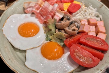 Round fried eggs with bacon, mushrooms, tomatoes on a plate on a table. Close-up