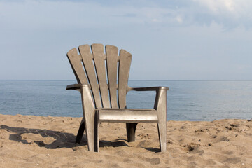 a brown composite plastic Adirondack style lawn chair on  a sandy beach near the water edge