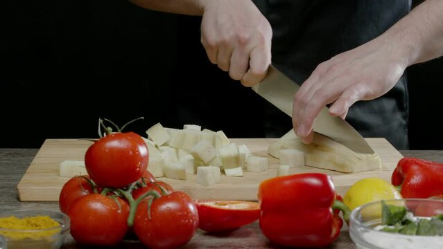 Cook cuts the white squash into large square pieces, while other vegetables are scattered around the kitchen. As the camera moves forward. Close up. Slow motion. 4k