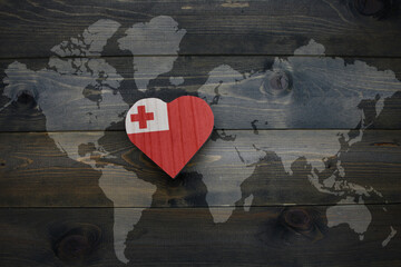 wooden heart with national flag of Tonga near world map on the wooden background.