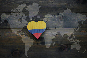 wooden heart with national flag of colombia near world map on the wooden background.