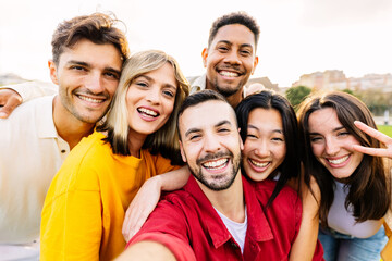 Young community concept with millennial friends having fun together outdoors. Diverse group of millennial people taking selfie portrait enjoying free time at city park.