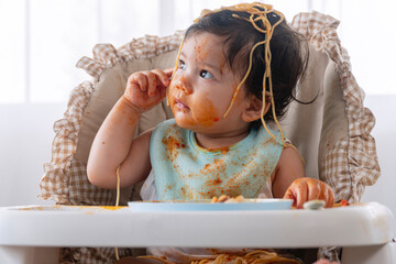 Adorable messy little child girl hungry use hand eating spaghetti sitting in high-powered chair at...