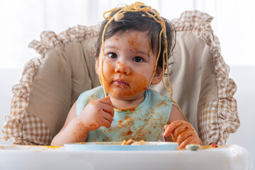 Adorable messy little child girl hungry use hand eating spaghetti sitting in high-powered chair at...