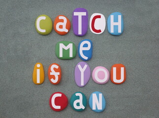 Catch me if you can, creative slogan composed with hand painted multi colored stone letters over green sand