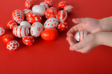 In the children's hands is an egg in red and white Easter eggs on a bright red background. A place to copy. Flat image, top view