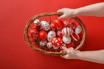 Easter backgrounds. The child's hands hold a basket with Easter red and white eggs on a bright red background. Copy space. Flat lay, top view