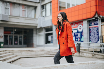A motivated businesswoman walks confidently in an urban setting, wearing a stylish red coat and...