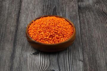 Red lentils in wooden bowl on wooden table background. Top view, copy space. Flat lay.