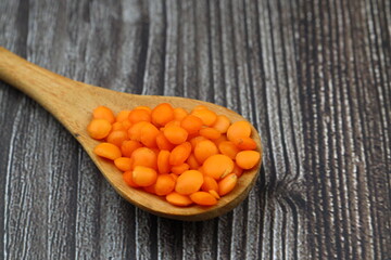 Red lentils in a wooden spoon on an old wooden table close-up. Vegetarian food.