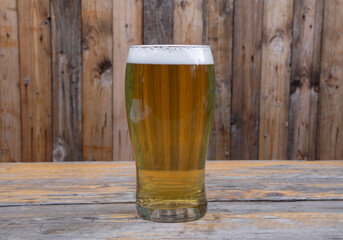 Closeup view of a full glass of honey golden beer with a rustic wooden background
