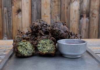 American food. Closeup view of spinach fritters with spicy sauce in a metal plate with a rustic wooden background