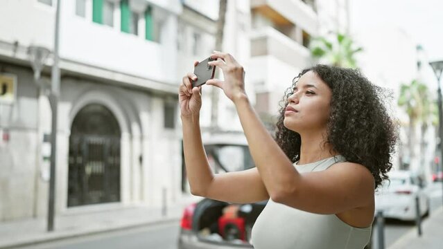 Confident, smiling young hispanic woman beautifully records video on smartphone in urban street