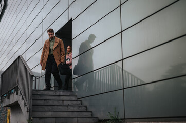 Two young professionals in casual business attire walking down the steps outside a contemporary...