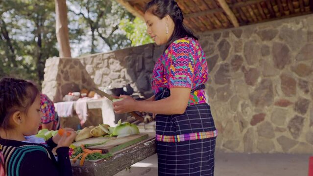 A Latina mother cuts vegetables and teaches her daughter how to eat them.