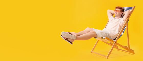 Young man resting in deck chair on yellow background