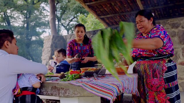 A mature Latina woman of the Mayan ethnic group leads the family to participate in the preparation of organic corn tamales.