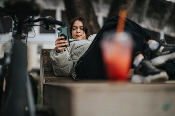 Casual young woman lying down near her bicycle in the park while browsing on her smart phone.