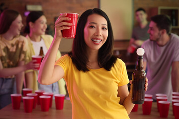 Young Asian woman with cup and ball for beer pong at party