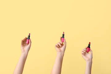 Female hands with lipsticks on yellow background