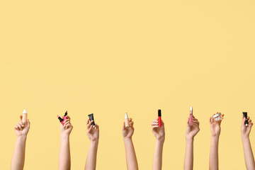Female hands with lipsticks, glitters and foundation on yellow background
