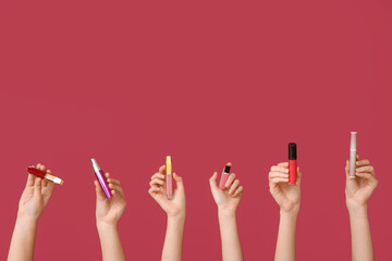 Female hands with lipsticks and mascara on dark red background