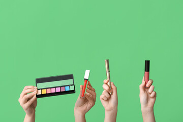 Female hands with eyeshadows palette, mascara and lipsticks on green background - obrazy, fototapety, plakaty