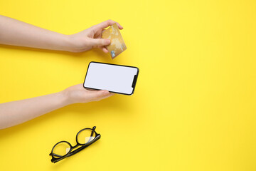 Online payment. Woman with smartphone, credit card and glasses on yellow background, top view....
