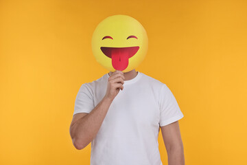 Man covering face with emoticon sticking out tongue on yellow background