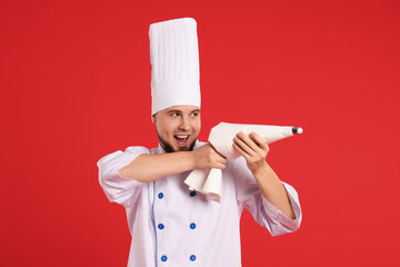 Happy professional confectioner in uniform having fun with piping bag on red background